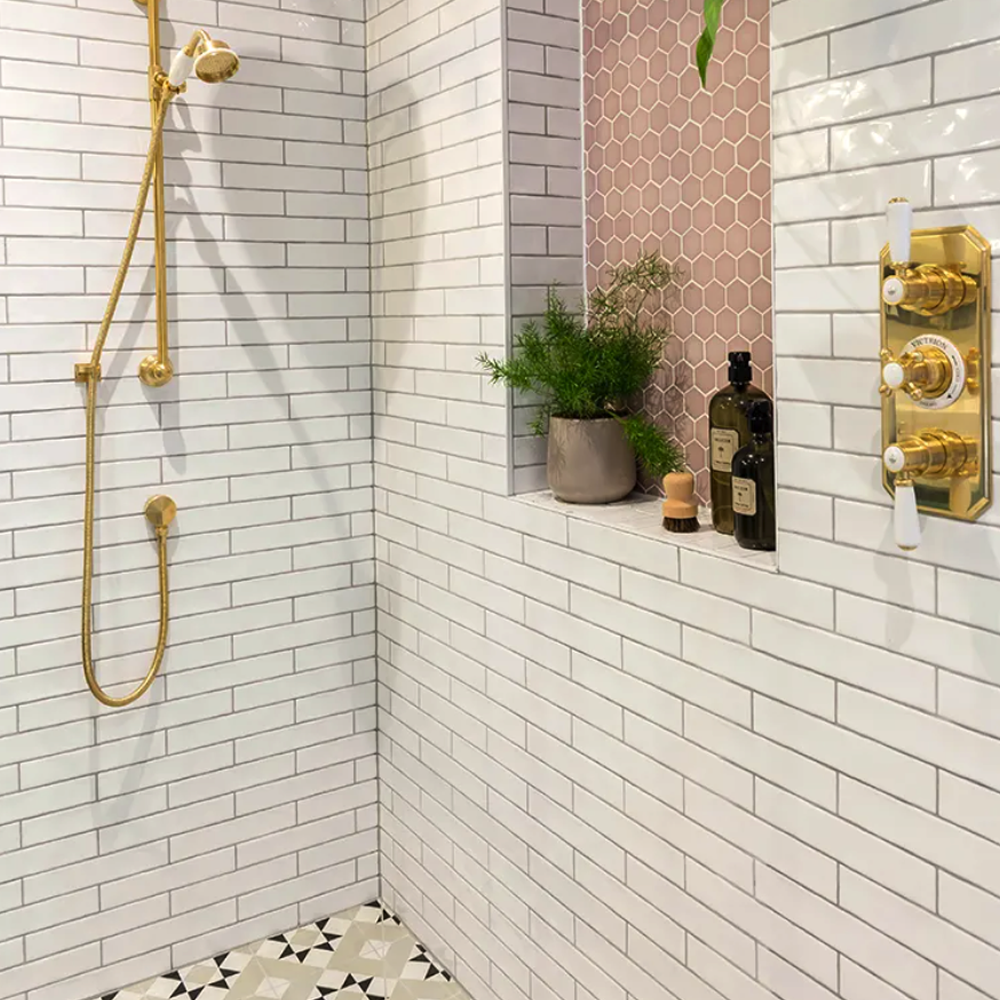 Shower area with white tiled walls, gold fixtures, and a small shelf with plants and bottles. Avebury Ceramic milk