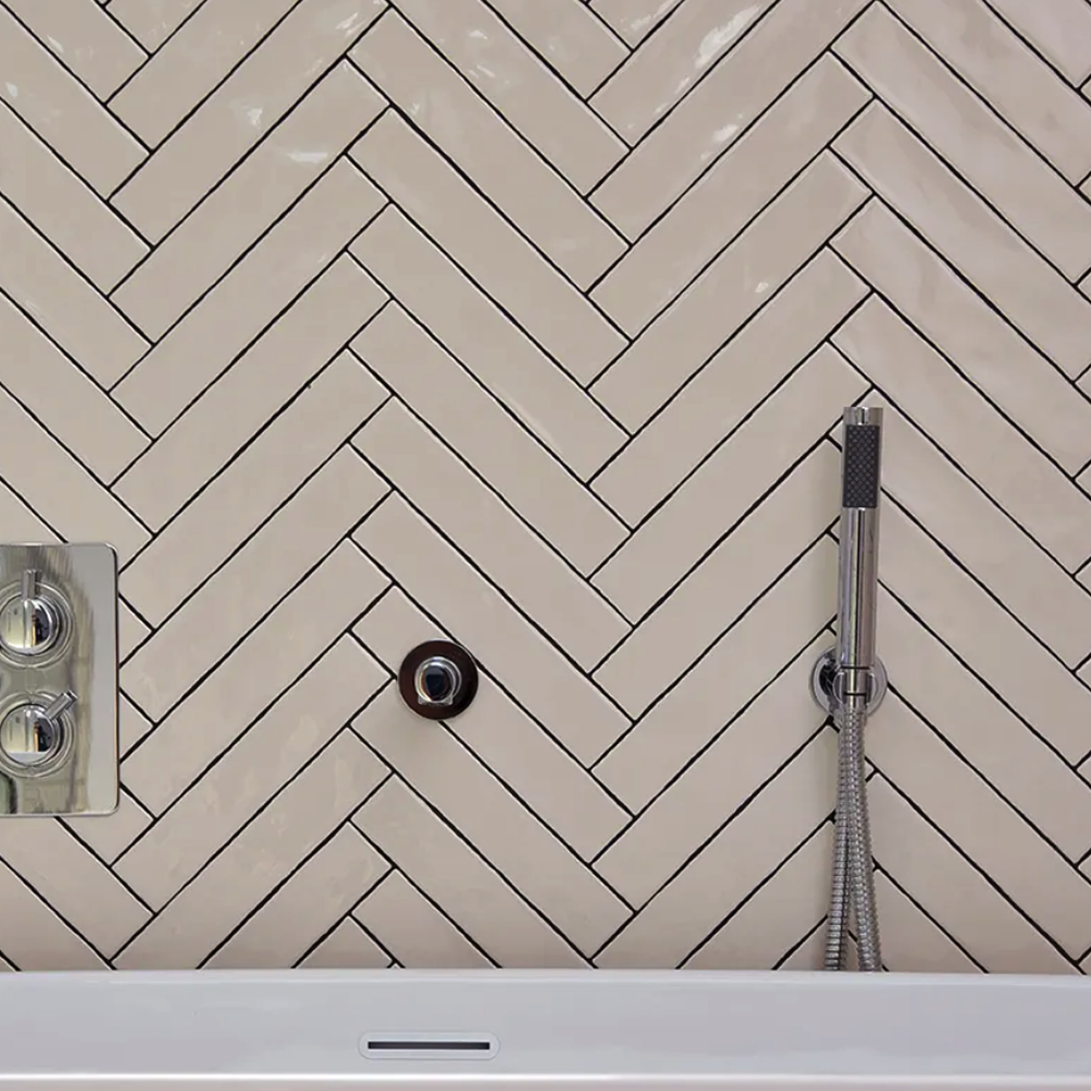 Tiled shower wall with a herringbone pattern and shower fixtures. plaster