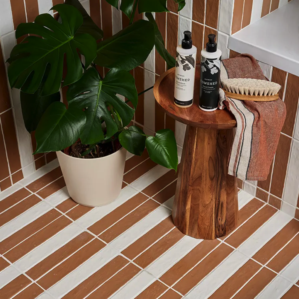 Bathroom setting with a wooden stool, plant, and bath products on a tiled floor.