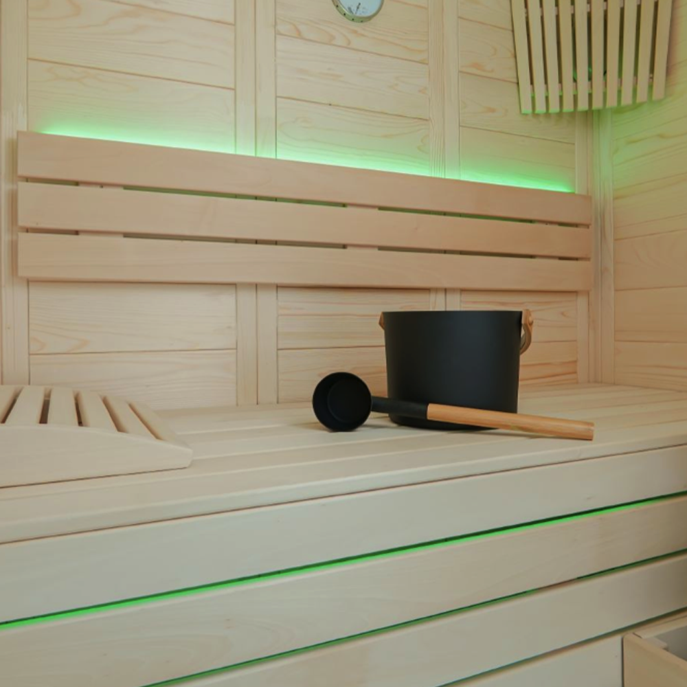 Black bucket and ladle on a wooden bench in a sauna with green LED lighting.
