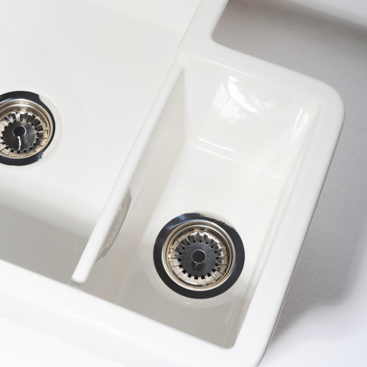 Close-up of a white kitchen sink with two drain holes on a light gray background