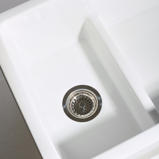 Close-up of a white kitchen sink with a silver drain cover.