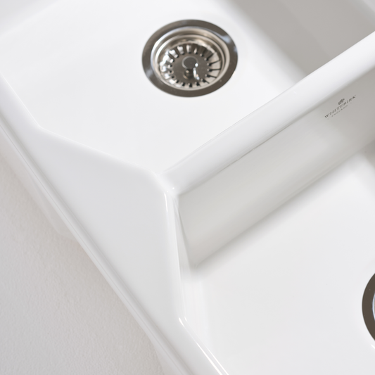 Close-up of a white kitchen sink with a silver drain.