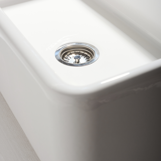 Close-up of a white kitchen sink with a silver drain.