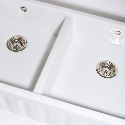 Close-up of a white kitchen sink with silver drain fixtures.