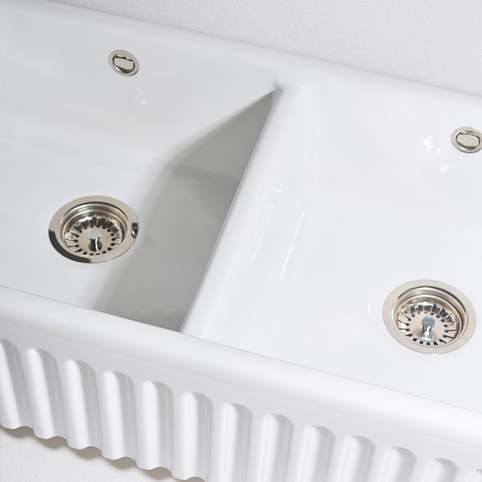 Close-up of a white kitchen sink with silver drain holes on a white background