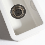 Close-up of a white kitchen sink with a metallic drain cover on a light gray background