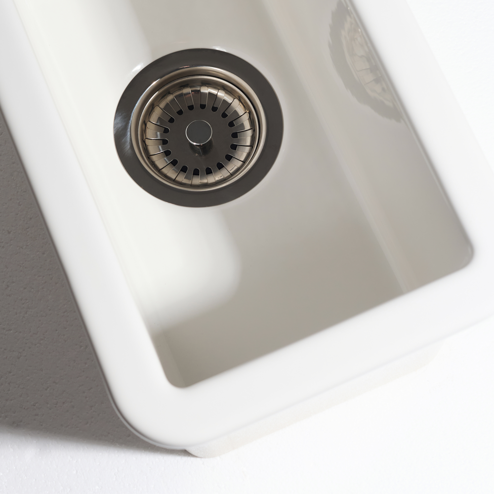 Close-up of a white kitchen sink with a metallic drain cover on a light gray background