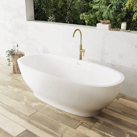 White freestanding bathtub with gold faucet on a wooden floor, surrounded by greenery.