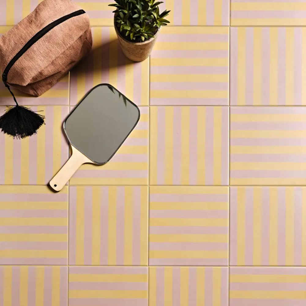 Decorative tiles with a hand mirror and plant on a yellow and pink striped floor.