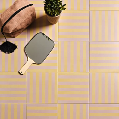 Decorative tiles with a hand mirror and plant on a yellow and pink striped floor.