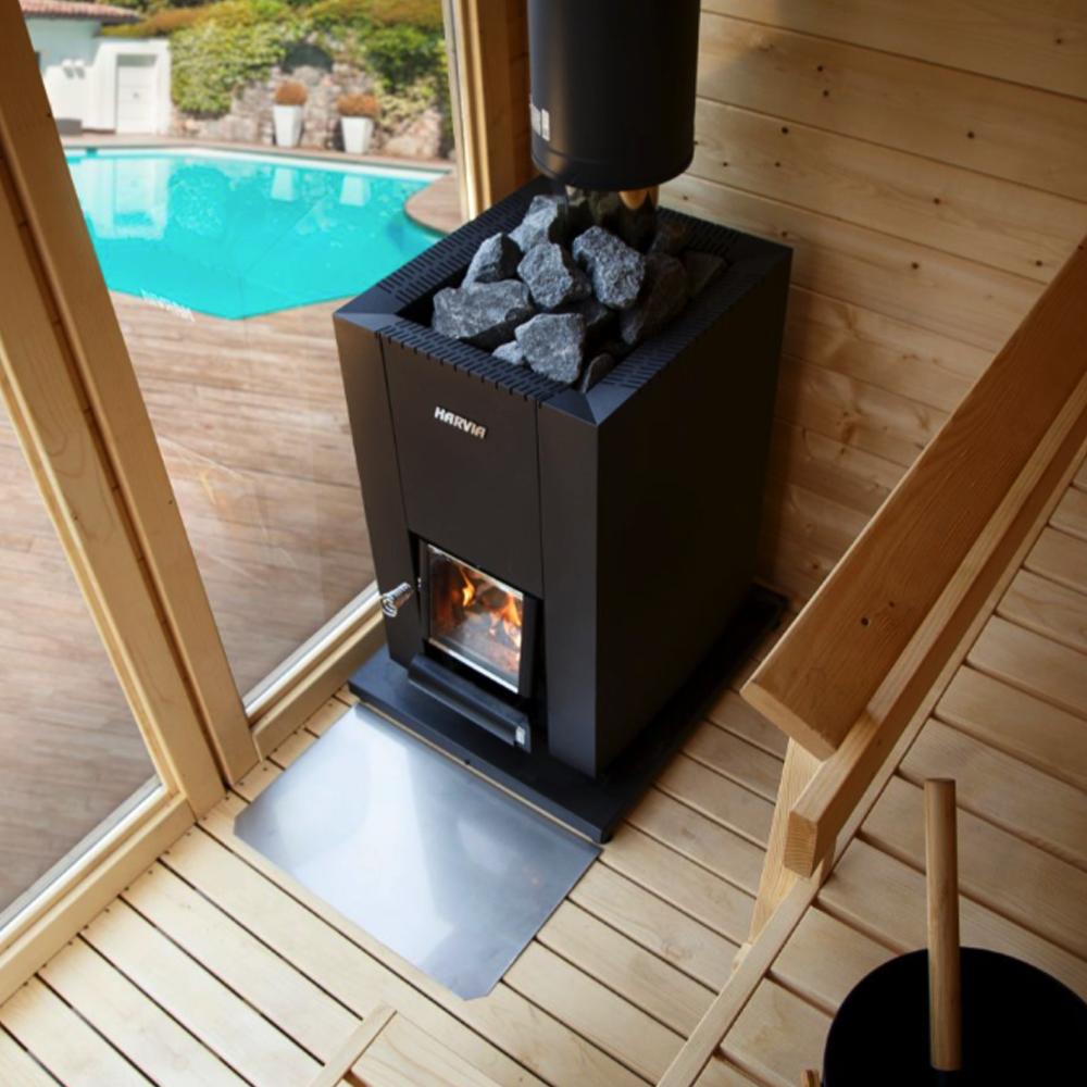 Black stove with stones inside, placed on a wooden floor next to a glass door showing a pool.