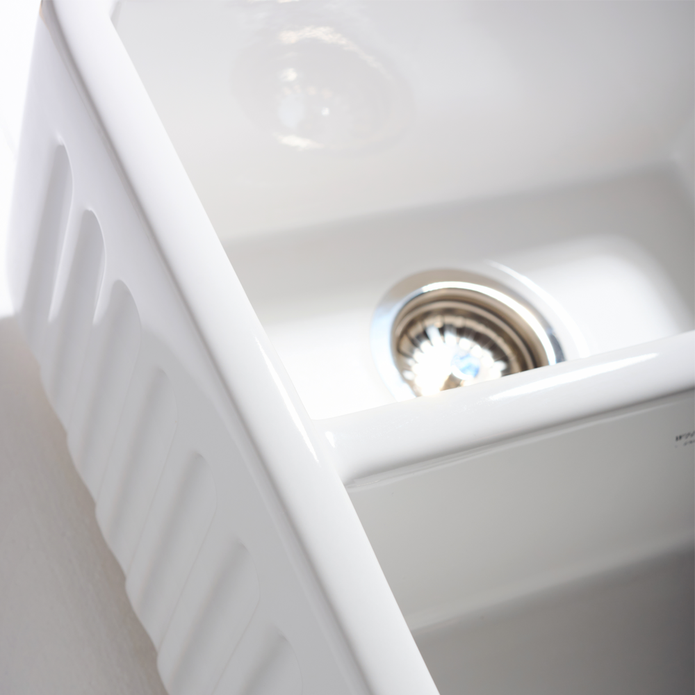Close-up of a white kitchen sink with a silver drain.