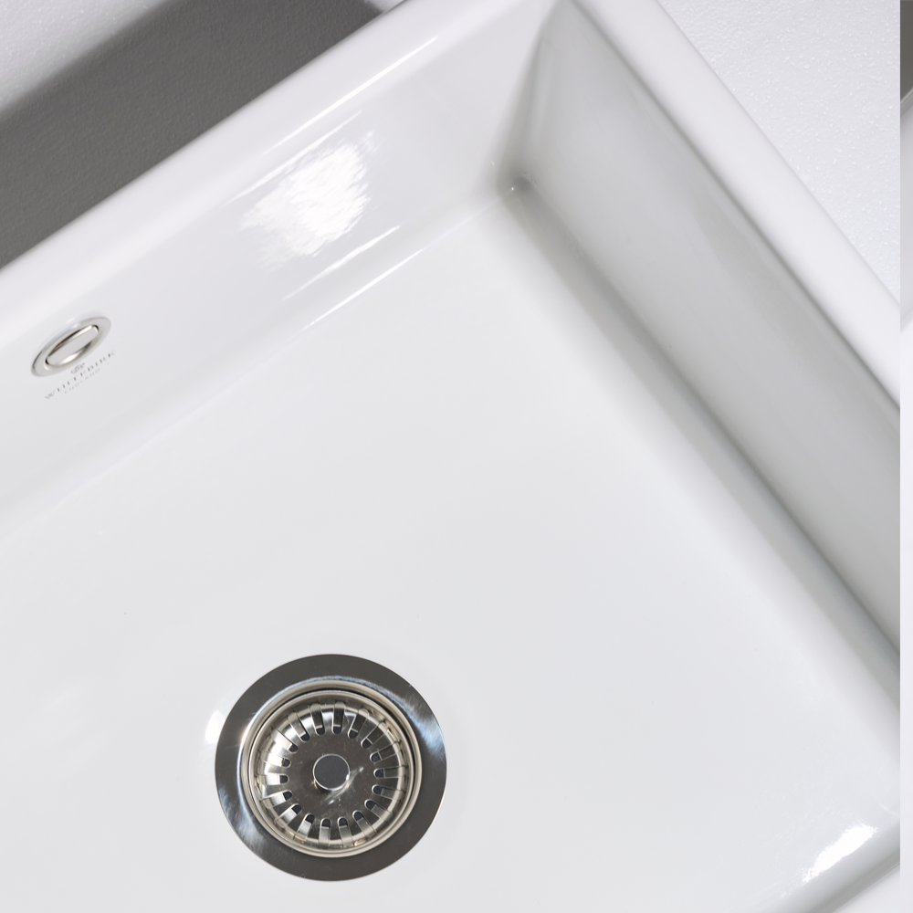 Close-up of a white kitchen sink with a silver drain cover.