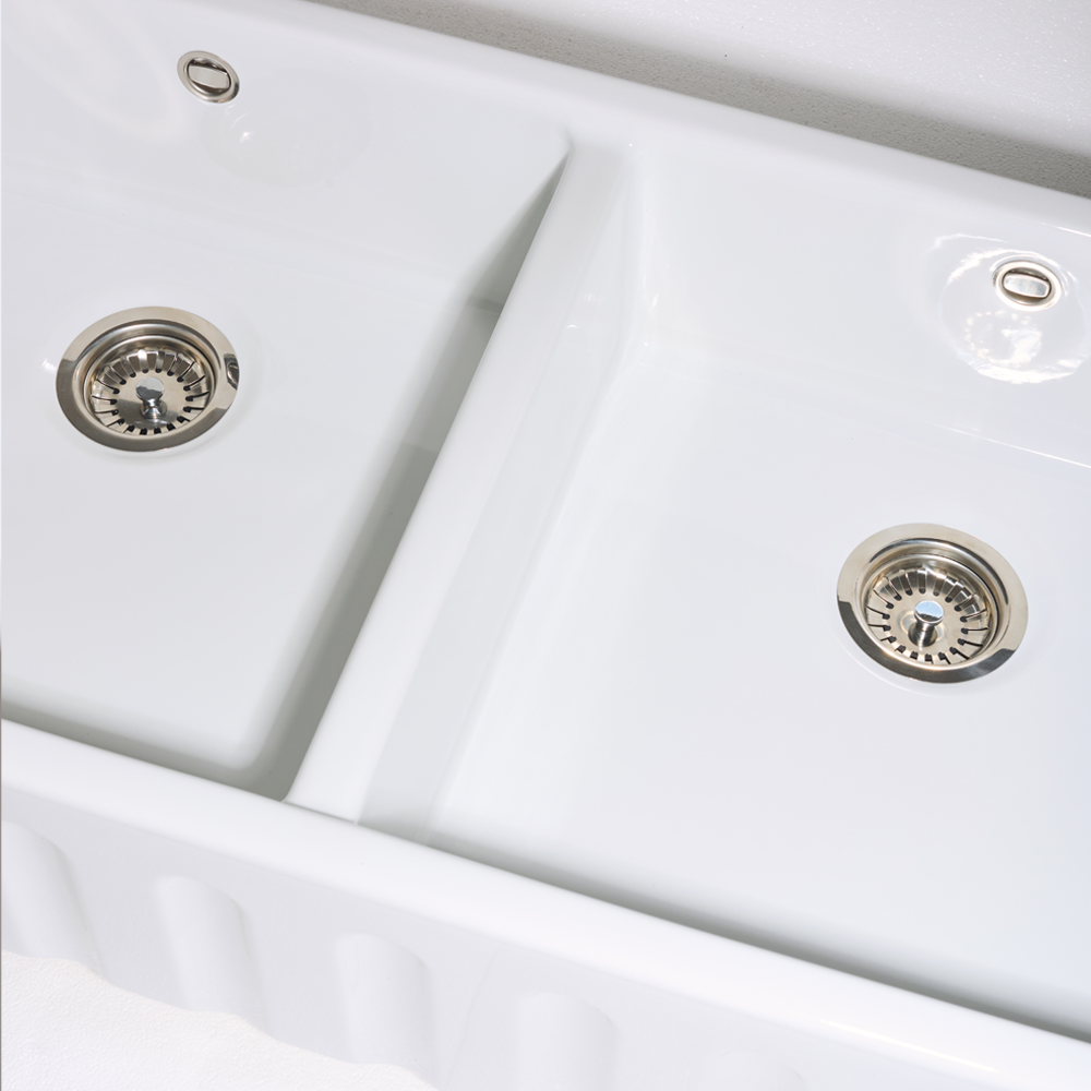 Close-up of a white kitchen sink with silver drain fixtures.