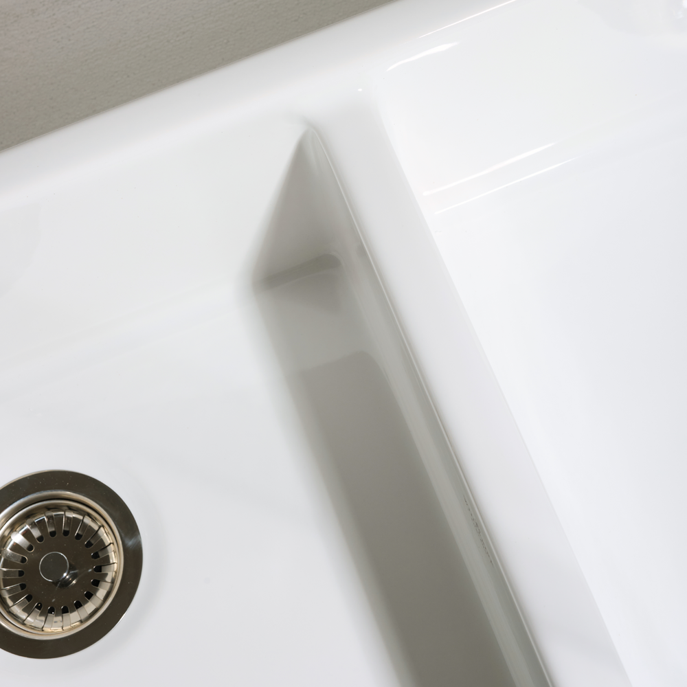 Close-up of a white kitchen sink with a silver drain cover.